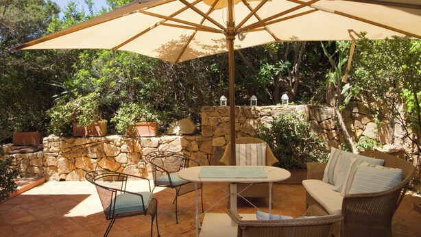 An outdoor patio with a stone wall, wicker furniture, and a large umbrella. - Porto Rotondo Center - free parking (Porto Rotondo)