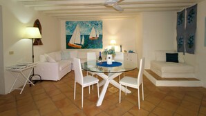 A dining area with a glass table and white chairs, a ceiling fan, a painting of sailboats, and a white sofa. - Porto Rotondo Center - free parking (Porto Rotondo)