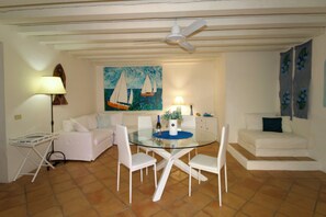 Ein Essbereich mit einem Glastisch und weißen Stühlen, einem Deckenventilator, einem Segelbootgemälde und einem weißen Sofa.