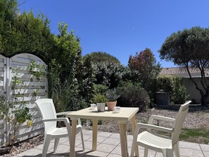 A patio with a table and chairs, surrounded by a garden with various plants and trees. - Vrbo Property (Saint-Denis-d'Oléron)