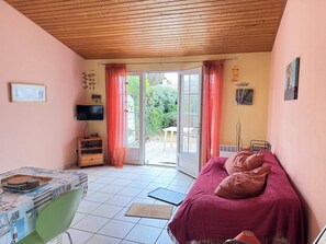 A bedroom with a bed, a desk, a chair, a TV, and a sliding glass door leading to an outdoor area. - Vrbo Property (Saint-Denis-d'Oléron)