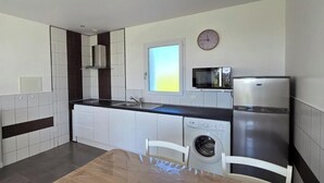 Una cucina moderna con mobili bianchi, un forno a microonde, un frigorifero, una lavatrice e un tavolo da pranzo con sedie.
