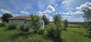 Una casa blanca amb teulada vermella, envoltada de vegetació i sota un cel serè.