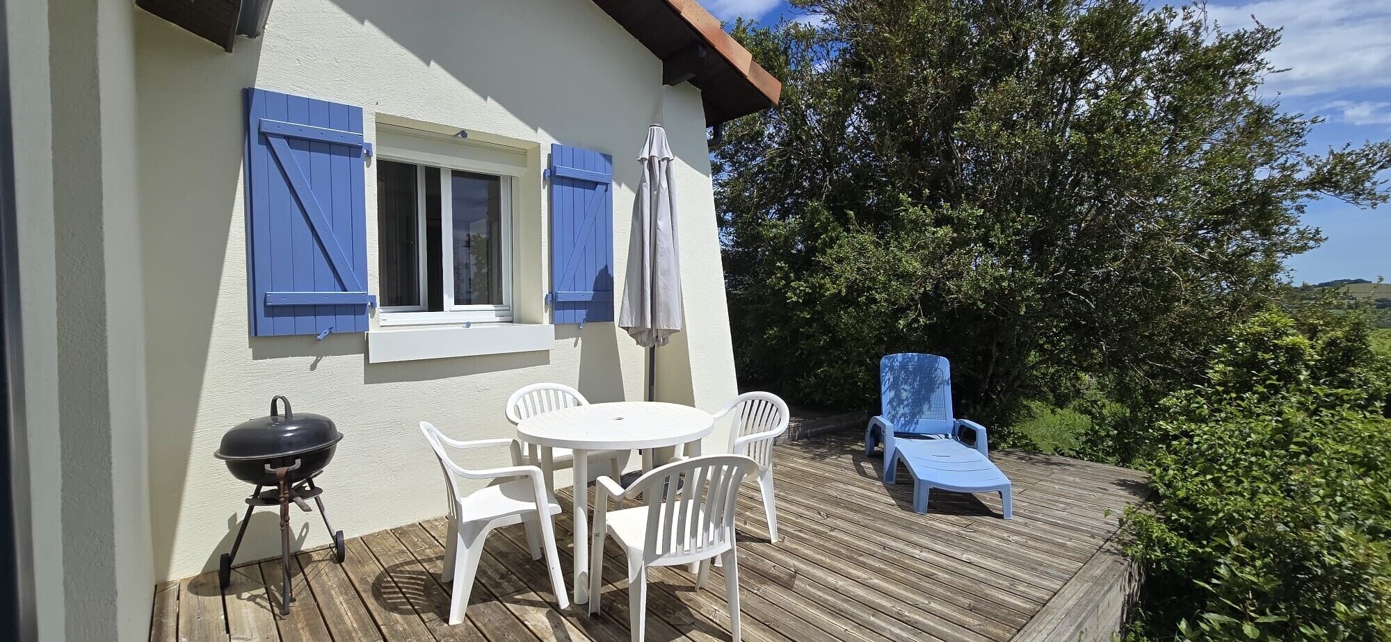 A patio with a table and chairs, a barbecue grill, and a lounge chair.