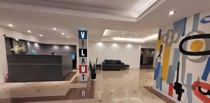 Eine moderne Hotelhalle mit Empfangstresen, einer Sitzecke und einem großen abstrakten Wandbild.
