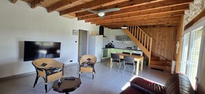 Un soggiorno con televisore, due poltrone in vimini, un tavolino, un divano e una scala che conduce a una cucina.