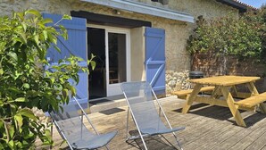 Eine Terrasse mit Holztisch und -stühlen, einem überdachten Sitzbereich und einer Steinmauer.