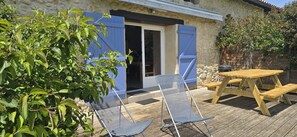 Une terrasse avec une table et des chaises en bois, un espace salon abrité et un mur en pierre.