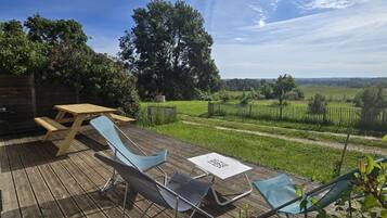 Une terrasse en bois avec une table et des chaises, un barbecue et une vue sur un vignoble.