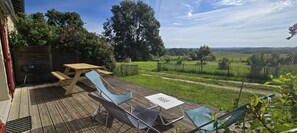 A wooden deck with a table and chairs, a barbecue grill, and a view of a vineyard. - Holiday Home “Gîte La Rapière En Armagnac” (Lauraët)