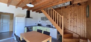 Une cuisine avec des poutres en bois, un escalier en bois et un coin repas comprenant une table et des chaises.