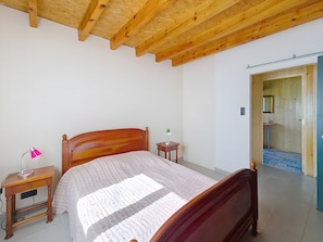 Un dormitorio con una cama de madera, una mesita de noche con lámpara y una pequeña mesa con lámpara.