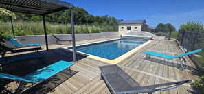 Un terrazzo in legno con piscina, sedie a sdraio e un edificio in pietra sullo sfondo.