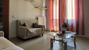 A living room with a sofa, a glass coffee table, a radiator, and a window with curtains. - Apartment 2 rooms - house Martina LuxRental Apartments (Pescara)