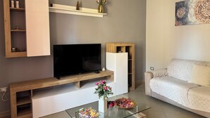 A modern living room with a flat-screen TV, wooden shelves, a glass coffee table, and a white sofa. - Apartment 2 rooms - house Martina LuxRental Apartments (Pescara)