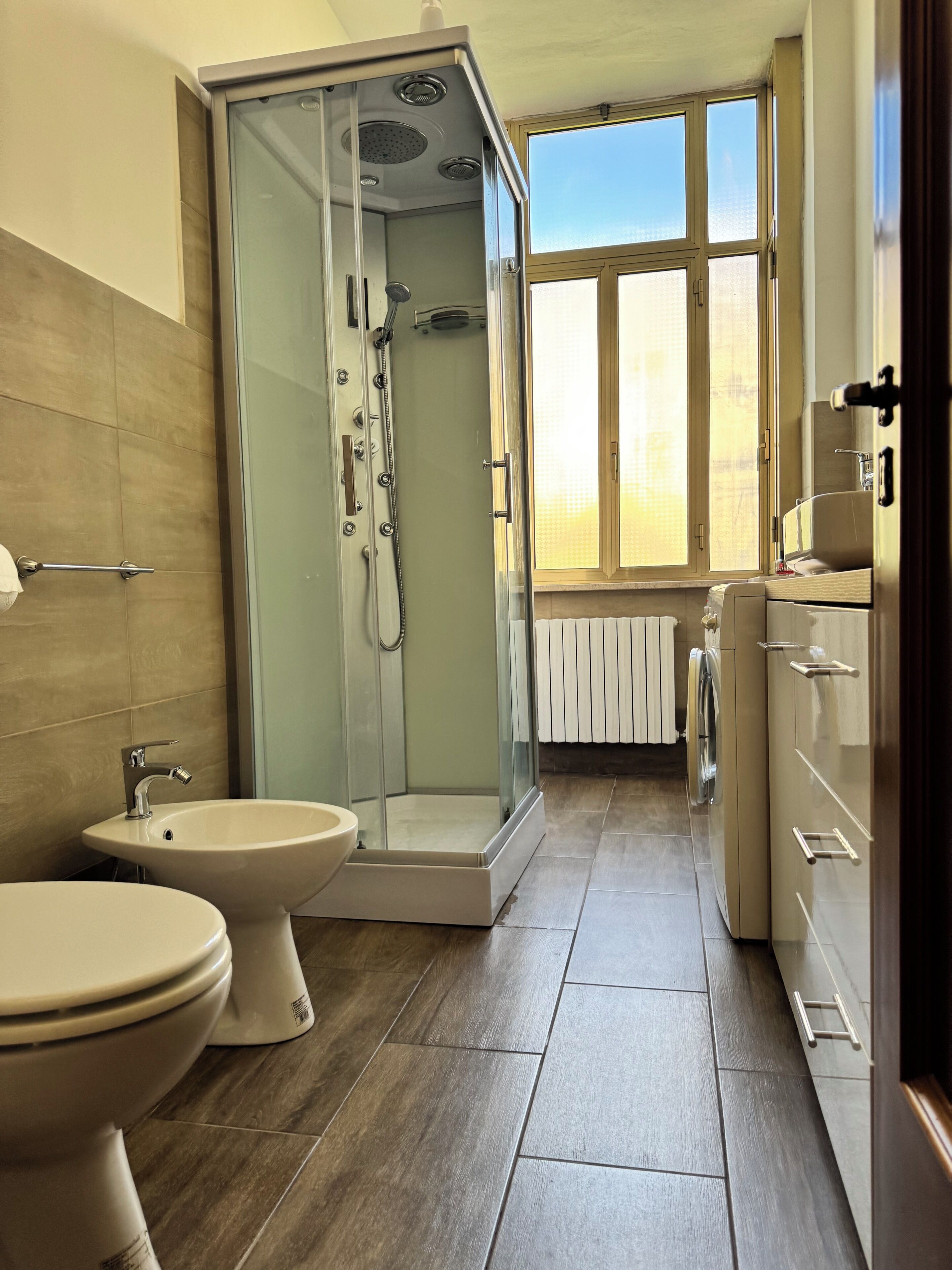 Een badkamer met een glazen douchecabine, toilet, bidet en raam met uitzicht.