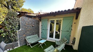 Um pátio com duas cadeiras estofadas verdes e uma mesa pequena, uma parede de pedra e uma porta de vidro deslizante.