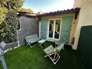 Eine Terrasse mit zwei grünen Polsterstühlen und einem kleinen Tisch, einer Steinmauer und einer Glastür, die sich öffnen lässt.