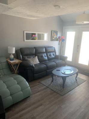 Un salon avec un canapé en cuir, un fauteuil vert, une petite table avec une lampe et un lampadaire.