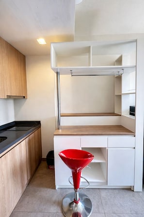 A compact kitchen with a built-in bench, a red bar stool, and a black trash bin. - Luxury Balcony View with Open Sky and Greenery (ตำบล หนองปรือ)