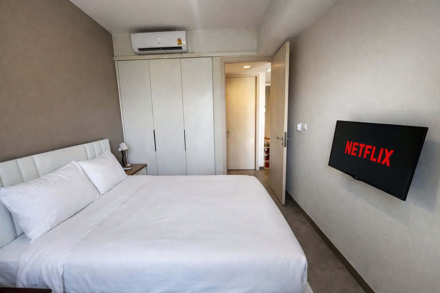 Camera d'albergo con un letto, un armadio, un condizionatore d'aria e una televisione a parete con il logo di Netflix.
