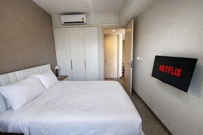 Quarto de hotel com cama, guarda-roupa, ar condicionado e televisão na parede exibindo o logotipo da Netflix.