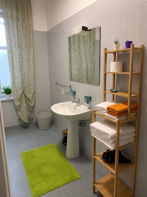 Une salle de bain avec un lavabo, un miroir, une étagère en bois avec des serviettes et un tapis vert.