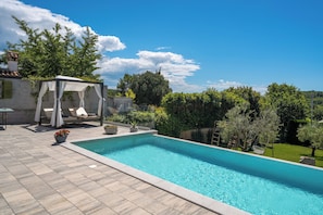 Une piscine agrémentée d’une pergola, de chaises longues et de plantes en pot.