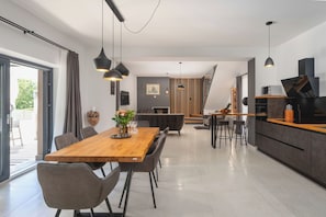Une cuisine moderne avec un plan de travail en bois, un coin repas comprenant une table et des chaises en bois, un éclairage suspendu et un escalier menant à un niveau supérieur.