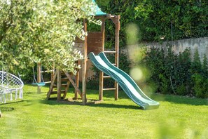 Une aire de jeux pour enfants avec un toboggan et des balançoires, installée dans un espace herbeux.