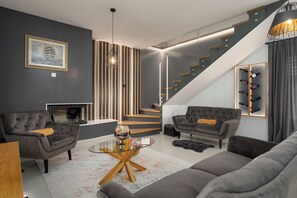 Una sala de estar moderna con chimenea, dos sofás, una mesa de centro de vidrio y una escalera.