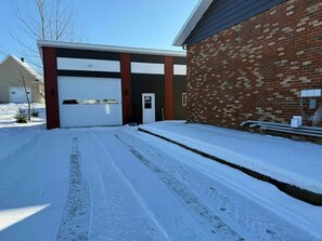 Ein verschneiter Weg führt zu einer Garage mit einer Ziegelwand und einer Garagentür.