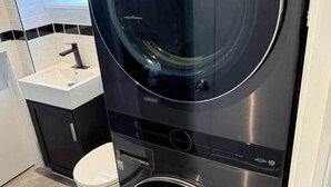 Una lavadora y secadora compactas en un baño con un lavabo y un inodoro blancos.