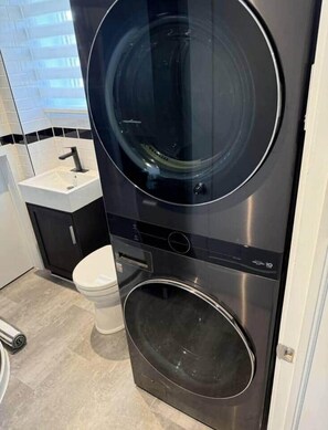Eine kompakte Waschmaschine und ein Trockner in einem Badezimmer mit einem weißen Waschbecken und einer Toilette.