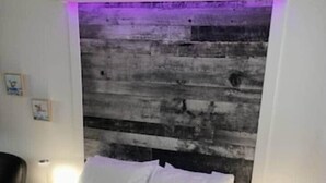 Un dormitorio con cama, dos mesitas de noche, cabecera y pared con textura.