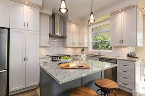 A modern kitchen with white cabinets, a granite countertop, a stainless steel refrigerator, and a large island with stools.