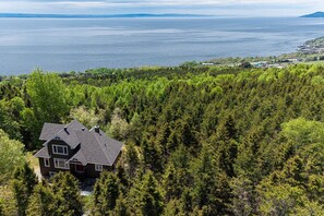 A house surrounded by dense forest with a view of a large body of water.