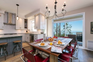 A modern kitchen with white cabinetry, a dining area with red chairs, and a view of the ocean.