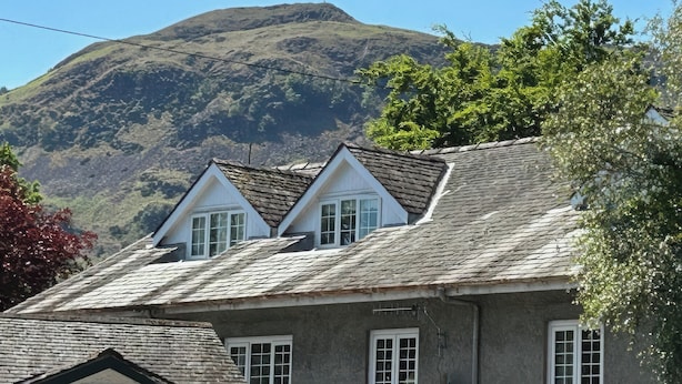 Ein Haus mit geneigtem Dach, mehreren Fenstern und Blick auf einen Berg im Hintergrund.