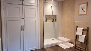 Ein Badezimmer mit bodengleicher Dusche, einem hölzernen Handtuchhalter und einem großen, weißen Kleiderschrank.