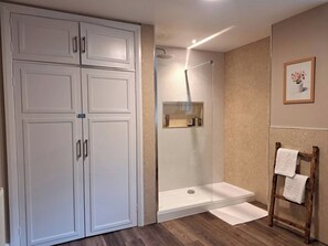 Ein Badezimmer mit bodengleicher Dusche, einem hölzernen Handtuchhalter und einem großen, weißen Kleiderschrank.