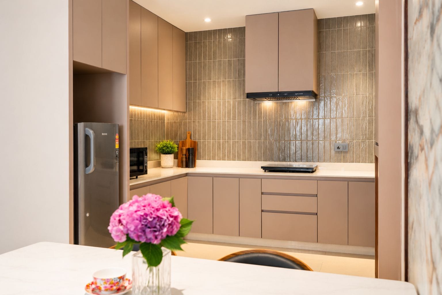 Cocina moderna con un refrigerador de acero inoxidable, un microondas y una estufa. Hay una planta en maceta sobre la encimera y un florero con flores en la mesa.