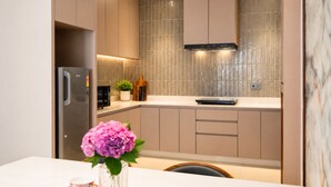 A modern kitchen with a stainless steel refrigerator, a microwave, and a stove. There is a potted plant on the counter and a vase with flowers on the table. - Maya Suites (Lalitpur)