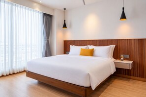 Habitación de hotel con una cama grande, cabecera de madera, mesitas de noche y vistas a través de cortinas translúcidas.