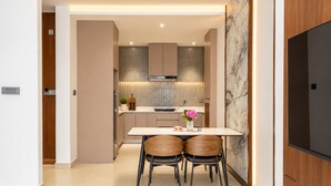 A modern kitchen with a dining area, featuring a marble backsplash, a built-in oven, and a flat-screen TV mounted on the wall. - Maya Suites (Lalitpur)