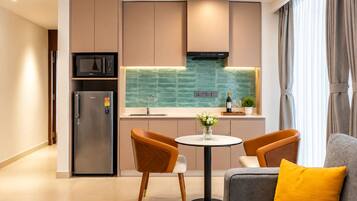 Cocina moderna con microondas integrado, refrigerador y salpicadero verde. Cuenta con una zona de comedor con dos sillas y una mesa pequeña.