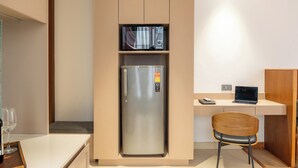 A compact kitchen with a built-in refrigerator, microwave, and a small dining area with a chair and table. - Maya Suites (Lalitpur)