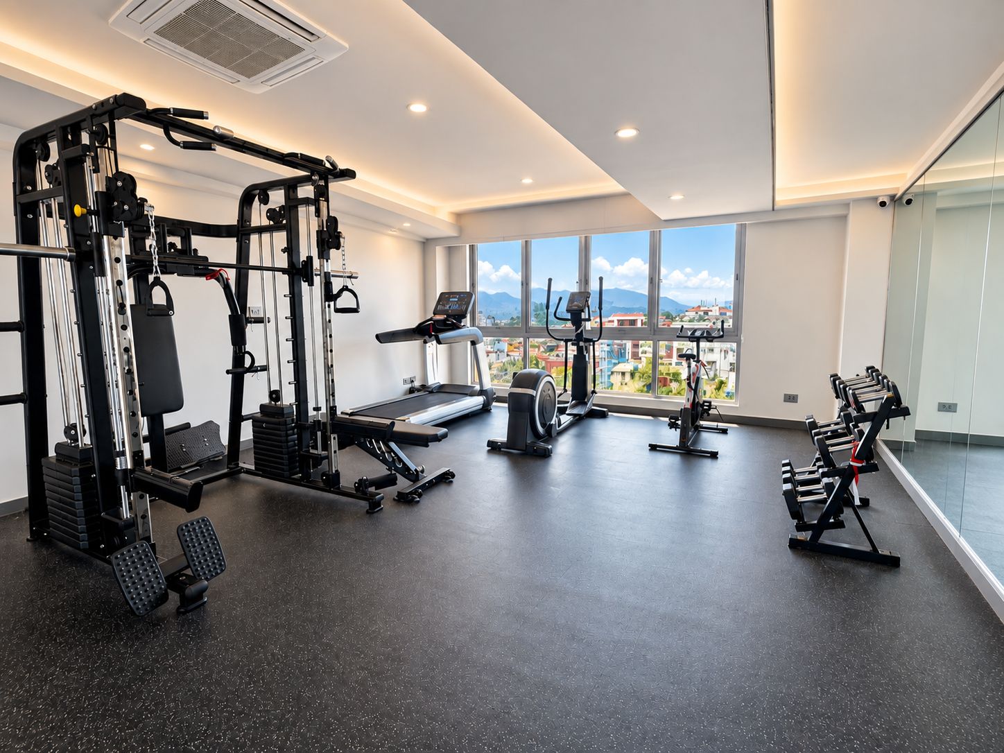 A gym with various exercise equipment, large windows, and a view of buildings and mountains.