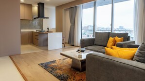 Ein modernes Wohnzimmer mit grauem Sofa, einem Couchtisch und Blick auf die Stadt durch große Fenster.