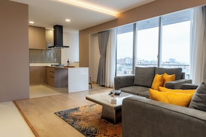 A modern living room with a grey sofa, a coffee table, and a view of the city through large windows. - Maya Suites (Lalitpur)